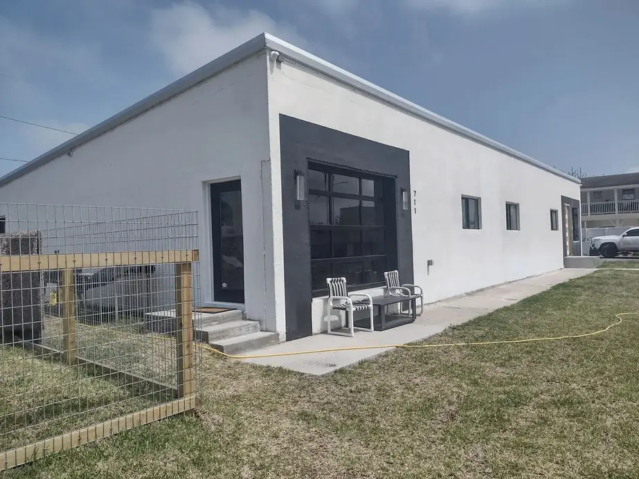 Finished white stucco building with a black-framed glass overhead door and a wire fence