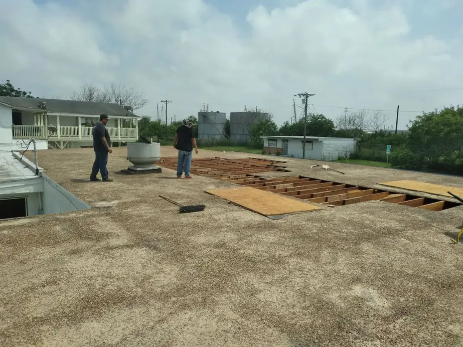 Two workers on the flat roof deck between open rafter bays